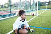 UK, Smiling female soccer goalie (12-13) sitting near goal