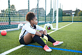 UK, Tired female soccer goalie (12-13) sitting at goal