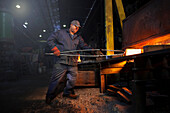 Forge worker removes red hot steel billet from furnace for forging into crank shaft
