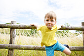 Porträt eines Jungen (18-23 Monate), der sich an einen Zaun im Feld lehnt
