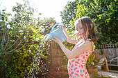 Mädchen (4-5) im Badeanzug gießt Wasser aus einer Gießkanne im Garten