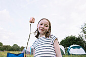 Porträt eines lächelnden Mädchens (4-5) mit Marshmallow am Stock auf dem Campingplatz
