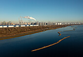 Netherlands, Oostvoorne, River with oil storage tanks and port cranes