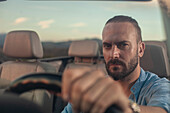 Portrait of man driving convertible car in landscape