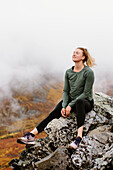 Kanada, Yukon, Whitehorse, Lächelnde Frau sitzt auf einem Felsen in nebliger Landschaft