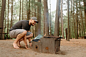 Canada, Yukon, Whitehorse, Man making fire on fire pit in campsite