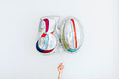 Studio shot of hand holding balloon in shape of number 30