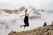 Kanada, Whitehorse, Frau springt über nebelverhangene Berglandschaft