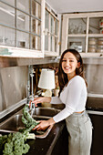 Lächelnde junge Frau wäscht Grünkohl in der Küchenspüle