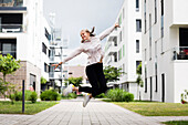 Lächelnde junge Frau beim Springen in moderner Umgebung