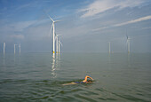 Niederlande, Friesland, Breezanddijk, Frau schwimmt in der Nähe von Windkraftanlagen