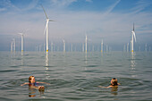 Niederlande, Friesland, Breezanddijk, Frau und Mädchen schwimmen in der Nähe von Windkraftanlagen