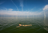 Niederlande, Friesland, Breezanddijk, Jugendliches Mädchen schwimmt in der Nähe von Windkraftanlagen