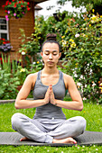 UK, London, Woman meditating on lawn in front of house