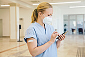 Österreich, Wien, Krankenschwester mit Gesichtsmaske benutzt Smartphone