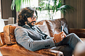 Italien, Geschäftsmann mit Smartphone sitzt auf Sofa in Kreativstudio