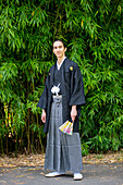UK, Porträt eines jungen Mannes im Kimono mit Fächer in einem Park