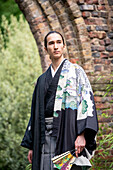 UK, Porträt eines jungen Mannes im Kimono mit Fächer in einem Park