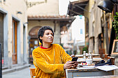 Italien, Toskana, Pistoia, Frau sitzt in einem Straßencafé und benutzt ihr Smartphone