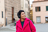 Italien, Toskana, Pistoia, Frau in rosa Mantel und Kopfhörern geht durch die Stadt