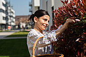 Lächelnde Frau sammelt Blätter von einer Hecke
