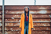 Italy, Milan, Portrait of woman in orange coat against rusty metal fence