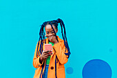 Italy, Milan, Woman with braids using smart phone against blue wall