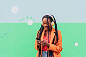 Italien, Mailand, Stylische Frau mit Kopfhörern und Smartphone vor einer Wand