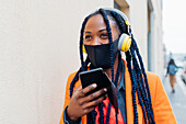 Italien, Mailand, Modische Frau mit Gesichtsmaske, Kopfhörern und Smartphone