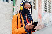 Italien, Mailand, Frau mit Kopfhörern und Gesichtsmaske hält Smartphone