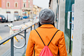 Italy, Milan, Rear view of woman in orange coat walking on sidewalk