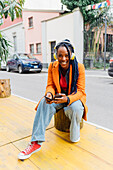 Italien, Mailand, Lächelnde Frau mit Kopfhörern und Smartphone in der Stadt