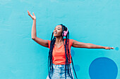 Italy, Milan, Young woman with headphones dancing in front of blue wall