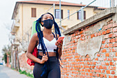 Italien, Mailand, Frau mit Gesichtsmaske und Sportkleidung beim Spaziergang in der Stadt