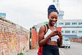 Italy, Milan, Smiling woman in sports clothing looking at smart phone in city