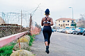 Italy, Milan, Rear view of woman with headphones jogging in city
