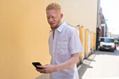 Deutschland, Köln, Albinomann im weißen Hemd hält Smartphone