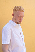 Germany, Cologne, Albino man in white shirt against yellow wall