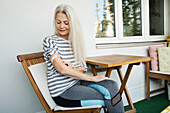 Österreich, Wien, Seniorin mit Pflasterverband am Arm auf Veranda sitzend