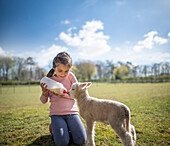 UK, North Yorkshire, Girl (6-7) feeding newborn lamb with bottle in organic farm