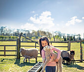 UK, North Yorkshire, Girl (6-7) holding lamb in organic farm