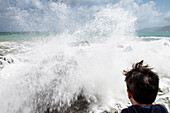 Junge (12-13) betrachtet Meereswellen, die gegen die Küste schlagen, Sizilien, Italien