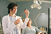 Ärztin bereitet Botox-Injektion vor, Patientin im Hintergrund
