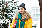 Portrait of smiling woman standing next to Christmas tree outdoors