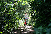 Boy riding bike on treelined footpath