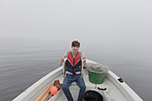 Junge (15-16) sitzt im Boot und hält einen Fisch