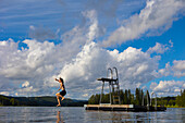 Boy (14-15) jumping off diving platform on lake