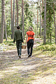 Two boys (14-15, 16-17) picking berries in forest, rear view