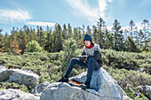 Junge (16-17) sitzt auf Felsen im Wald