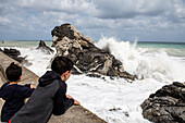 Italien, Sizilien, Junge schaut auf krachende Meereswellen